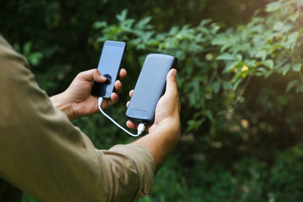 Tourist with smartphone and battery charger is walking in the summer forest.