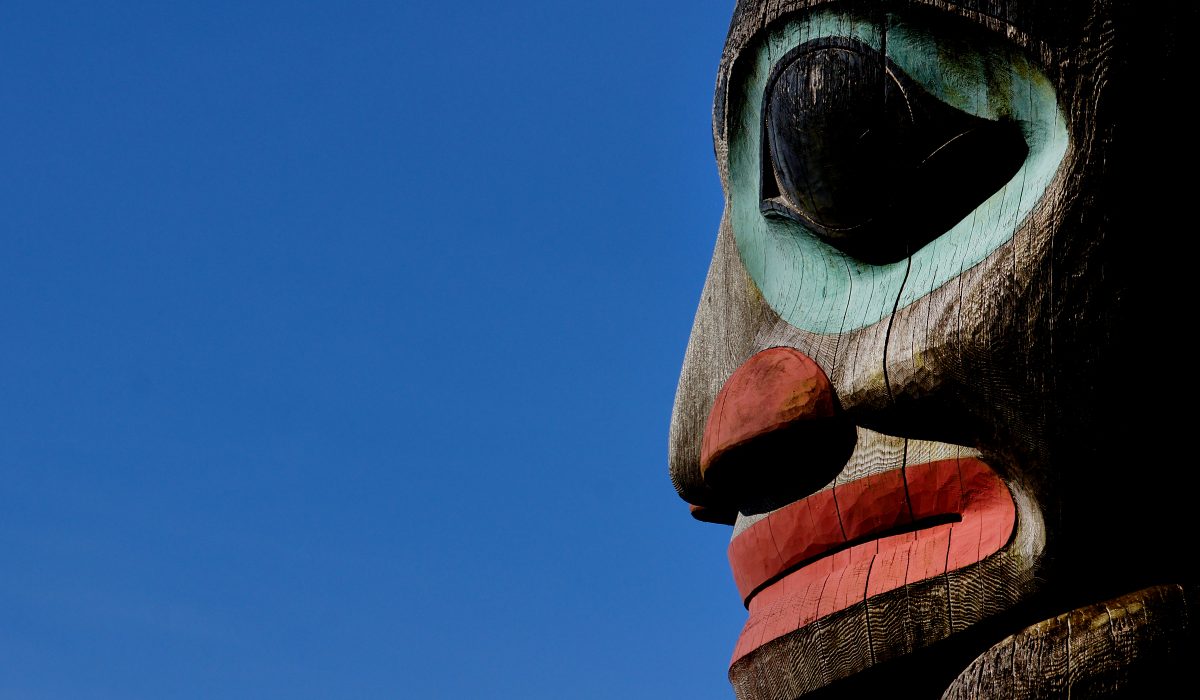 Close up shot of a totem pole with a face carved on it, painted in hues of red and blue, one of the best souvenirs from Alaska.