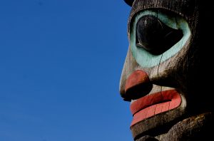 Close up shot of a totem pole with a face carved on it, painted in hues of red and blue, one of the best souvenirs from Alaska.