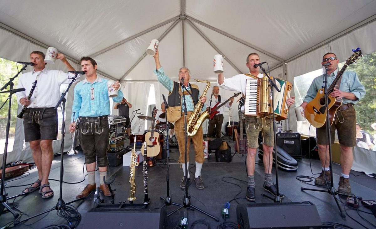 Band performers raising beer steins on stage during Breckenridge Oktoberfest near me in Colorado.