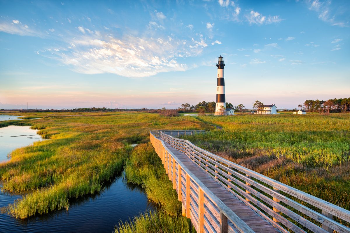 Wide shot of a marshland during early morning with a lighthouse in the background in Outer Banks, North Carolina.