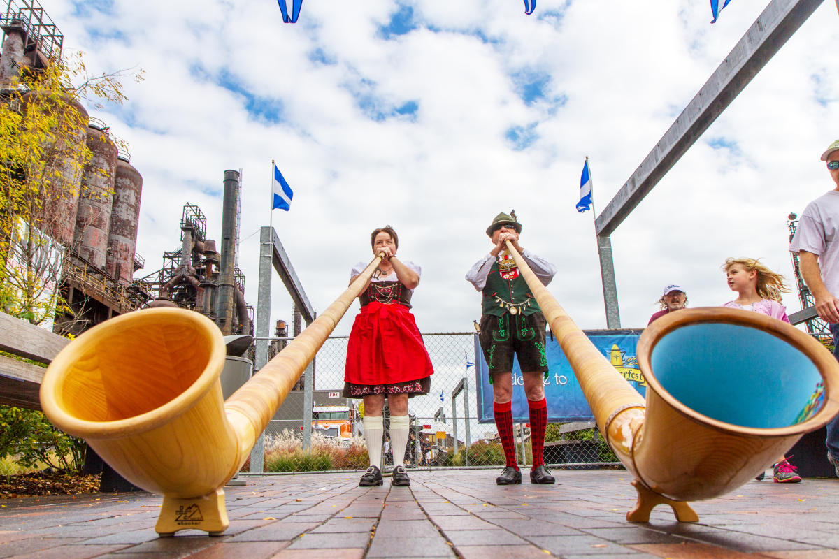 Man and woman playing the alphorn while wearing traditional German clothing.