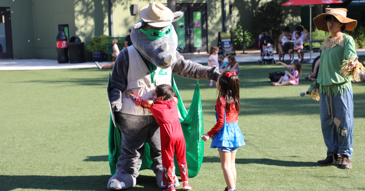 Kids interacting with mascots at San Antonio Zoo during early Halloween celebrations. 