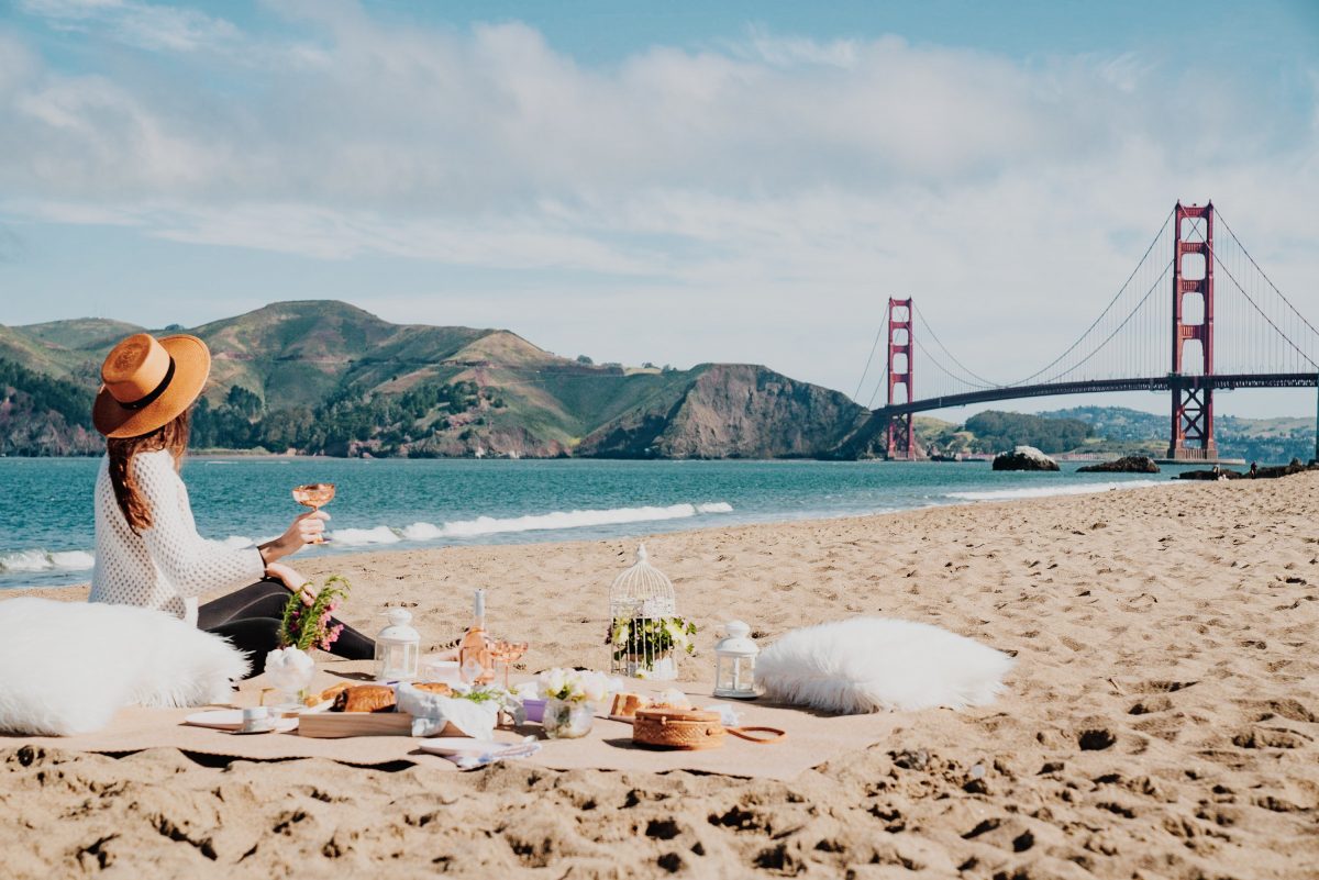 Woman picnicking by the beach in San Francisco with the Golden Gate Bridge in the background.