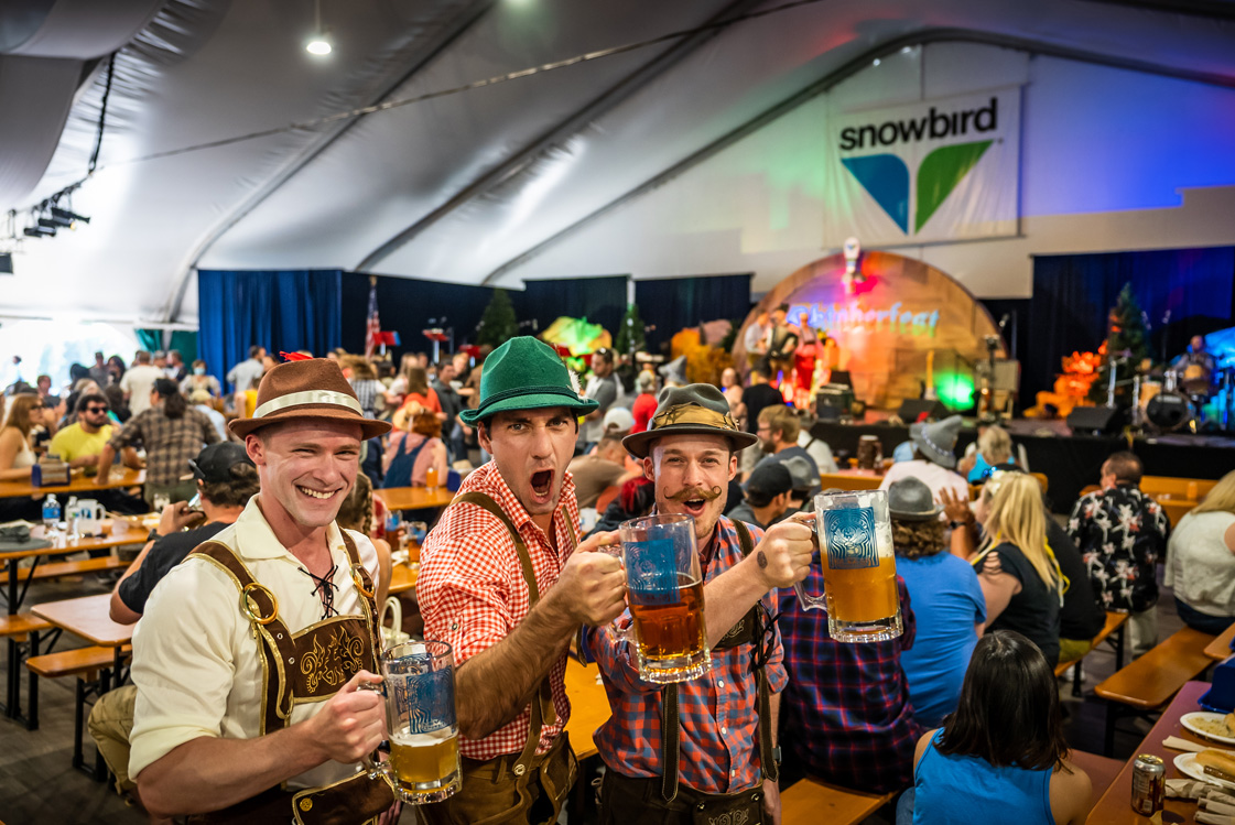 Three men wearing lederhosen and holding beer steins during Snowbird Oktoberfest; Oktoberfest near me in Utah.