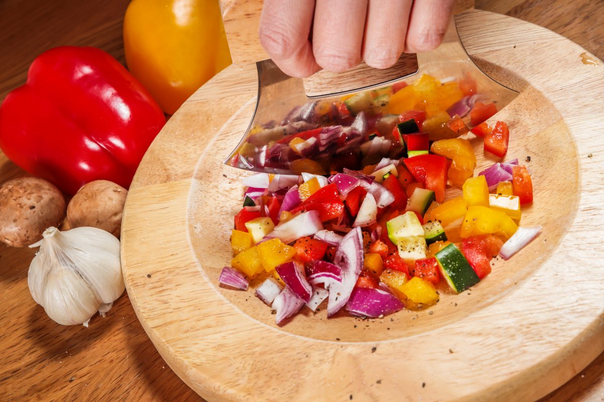 Close up shot of an ulu knife chopping vegetables on top of a wooden bowl, one of the best souvenirs from Anchorage, Alaska.