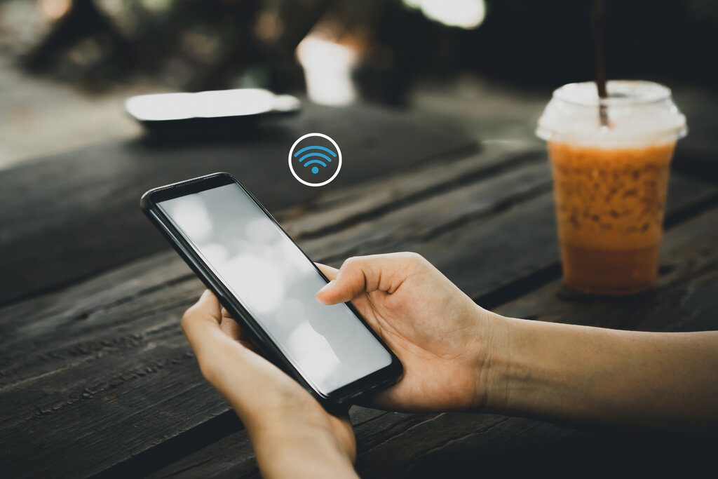 Woman hand using smart phone with wifi icon abstract background at coffee shop colorful bokeh light.