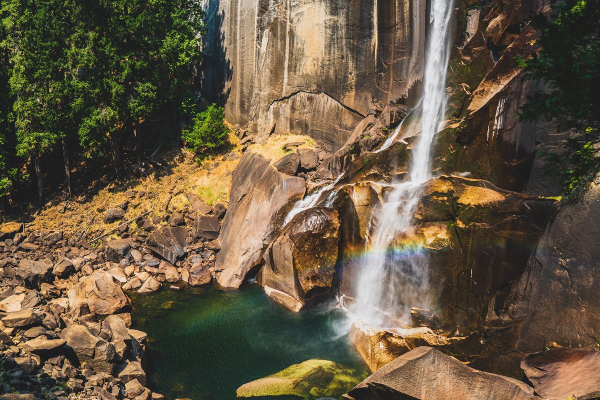 Waterfalls against a rocky mountain with a small rainbow.