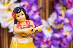 hula girl figurine with a flower lei in the background, some of the best hawaii souvenirs to buy.