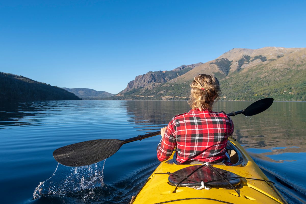 Woman canoeing in a body of water with a mountain range and greenery in the background.