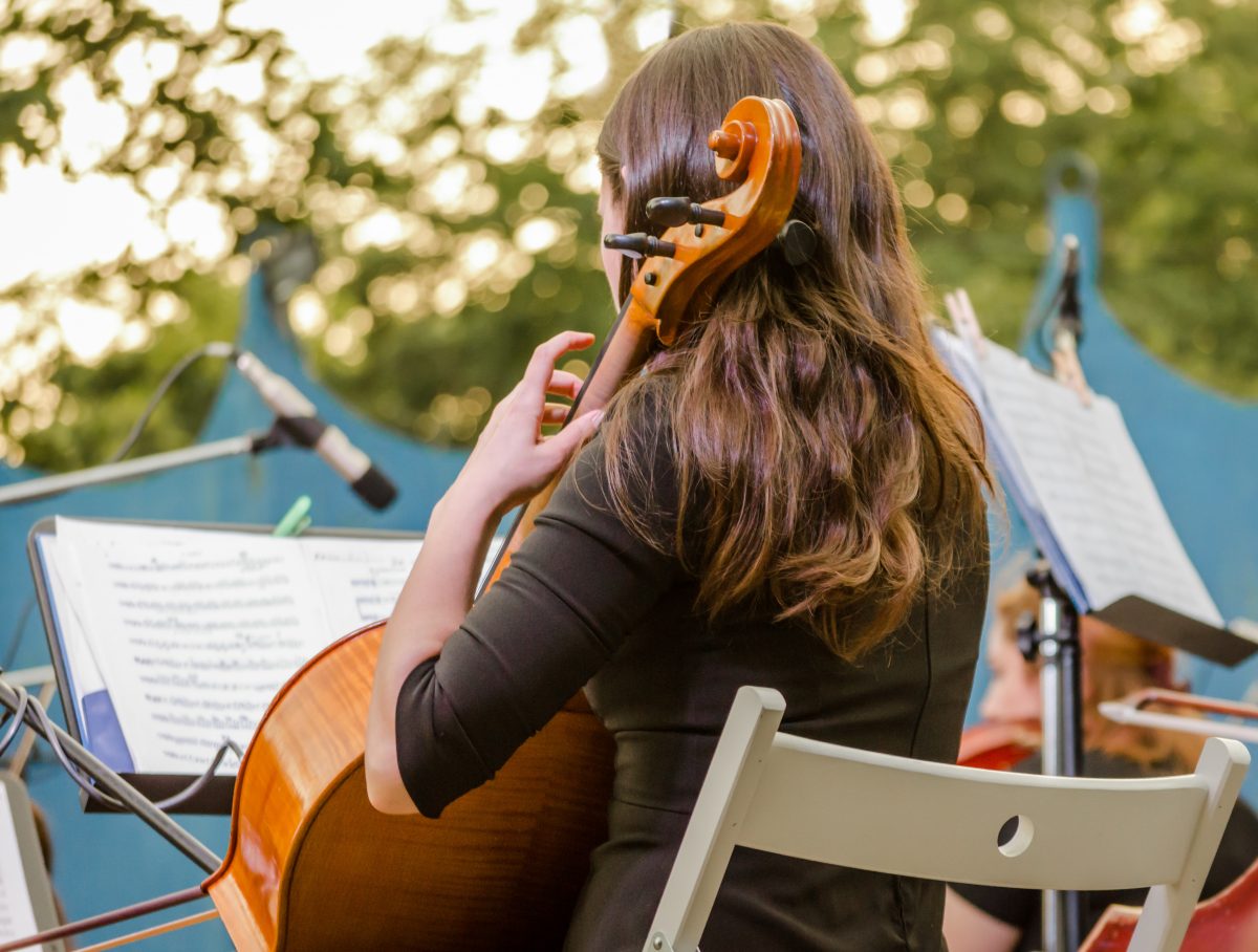 perspective shot of a cello player and her sheet music during an outdoor concert.