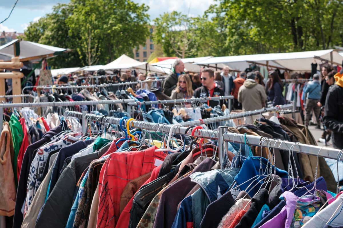people browsing through the clothing racks of an outdoor bazaar.