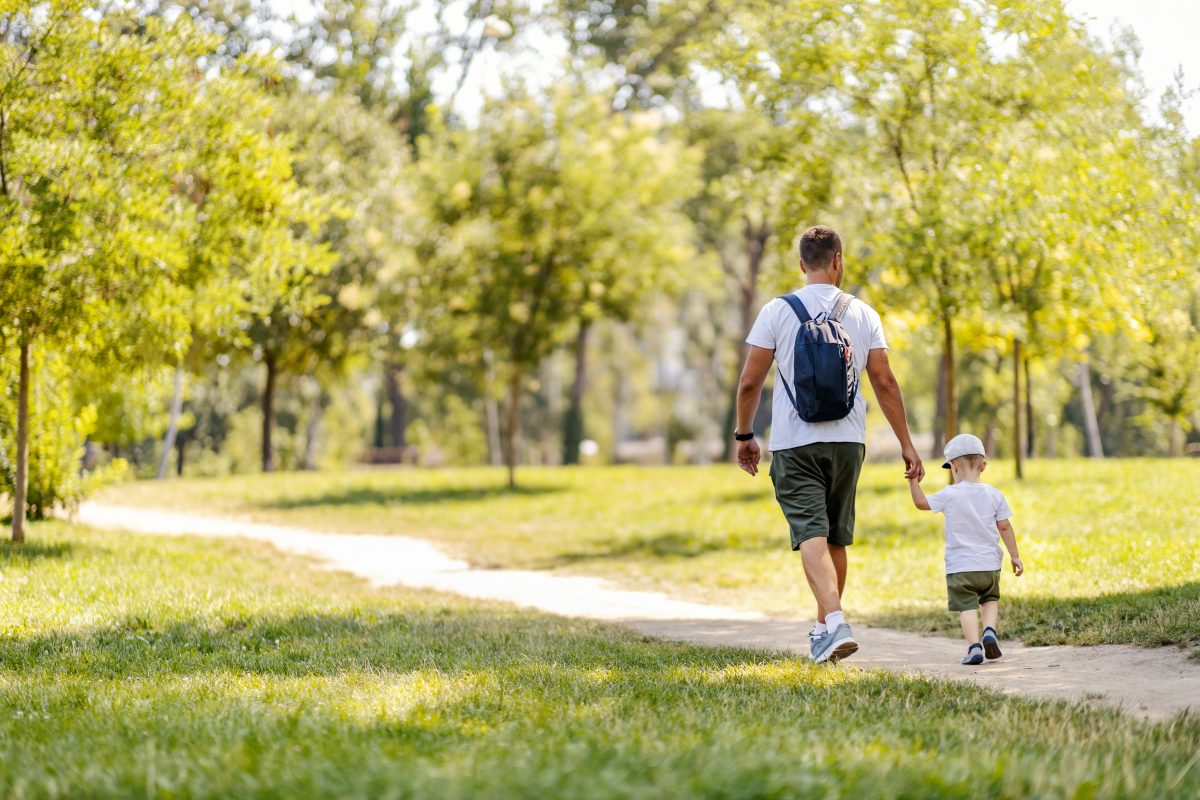 Adult man and small child walking along a paved path surrounded by greenery.