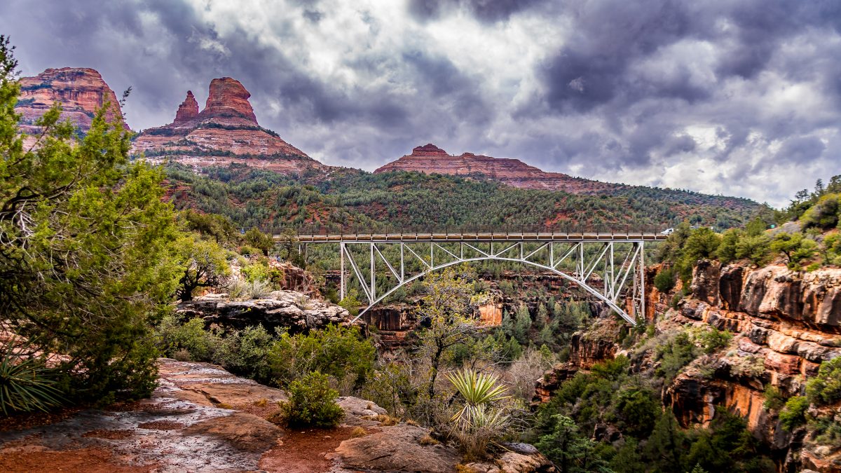 Wide shot of a bridge surrounded by red rocks and greenery within Oak Creek Canyon.