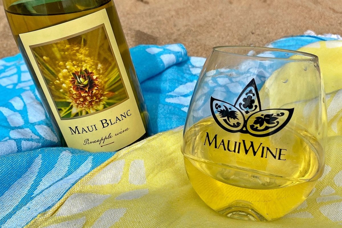 bottle and glass of pineapple wine laid out on a beach blanket, one of the top souvenirs from maui, hawaii. 
