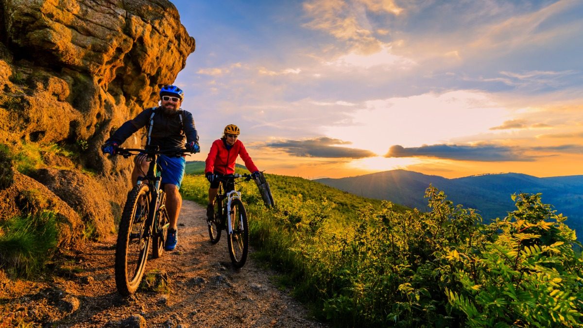 Mountain biking Mountain biking women and man riding on bikes at sunset mountains forest landscape