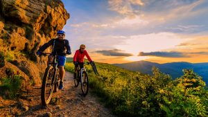 Mountain biking women and man riding on bikes at sunset mountains forest landscape