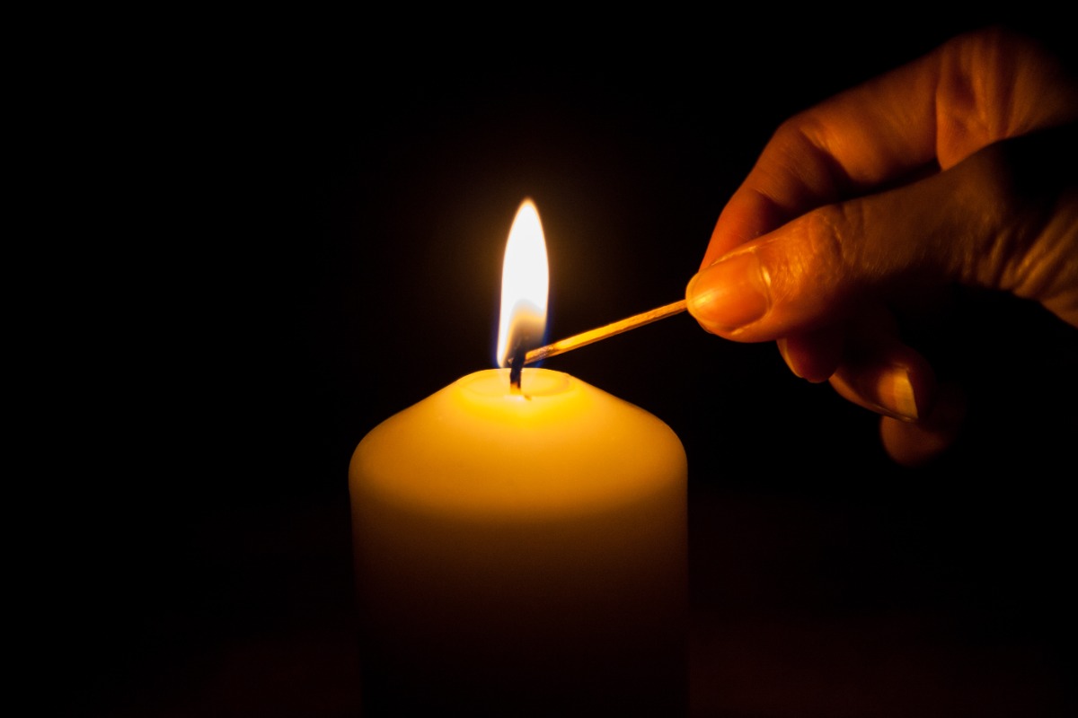 hand with matchstick lighting a candle