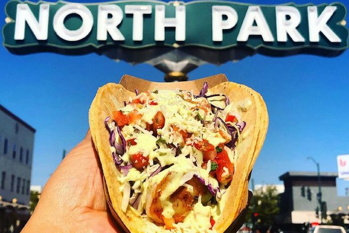 hand holding a taco from lucha libre in front of a north park sign in san diego.