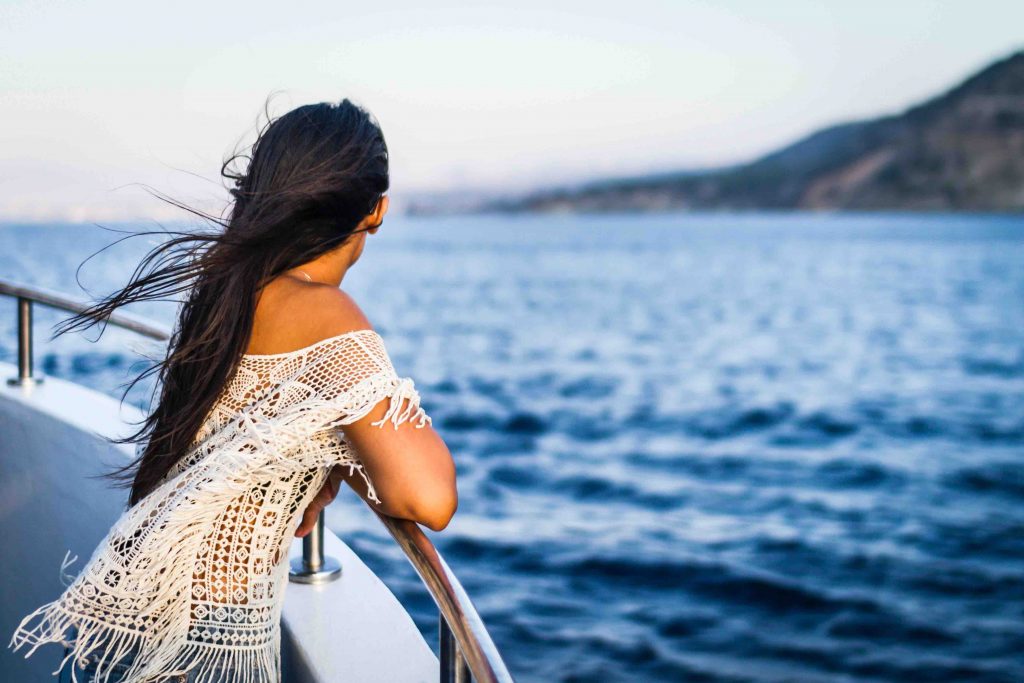 a back view shot of a women with long hair look out to the sea while on a cruise deck 
