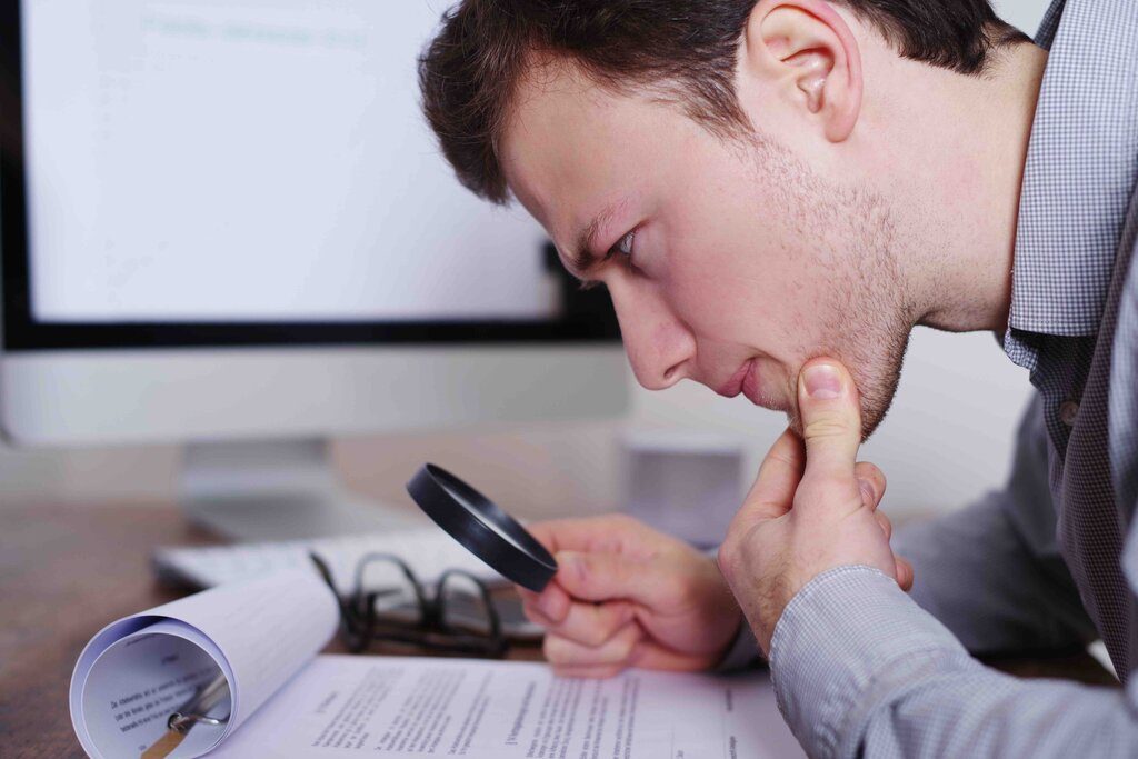 a side view shot of man holding a magnifying glass as he reads a document carefully