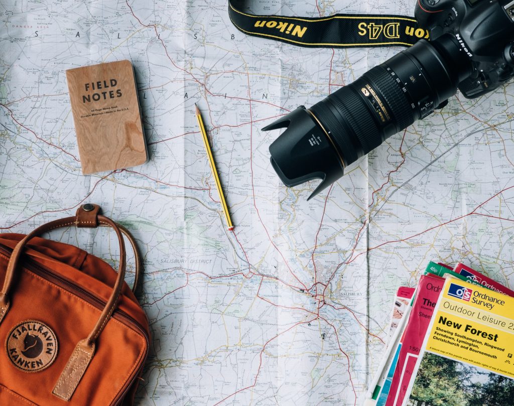 a flat lay image of a map, notebook, a backpack, a camera and a travel guide book