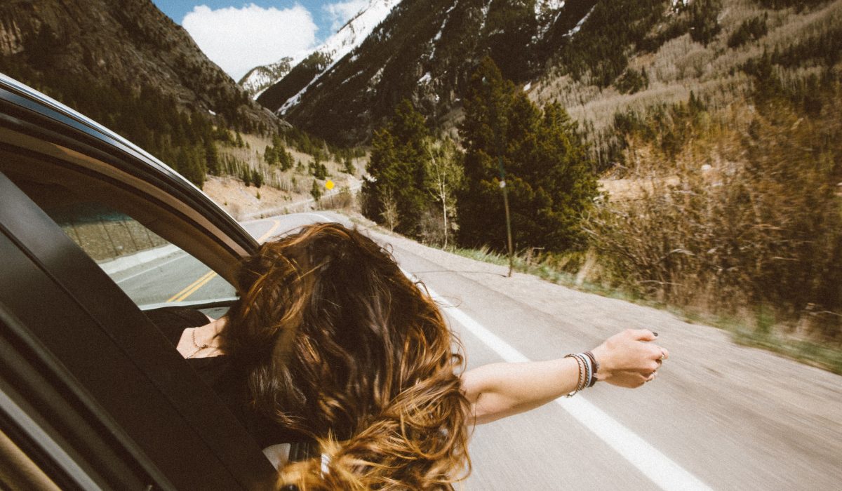 a back view shot of a girl sticking her hand out of a car during a road trip