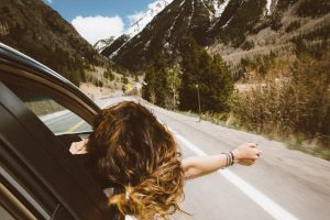 a back view shot of a girl sticking her hand out of a car during a road trip