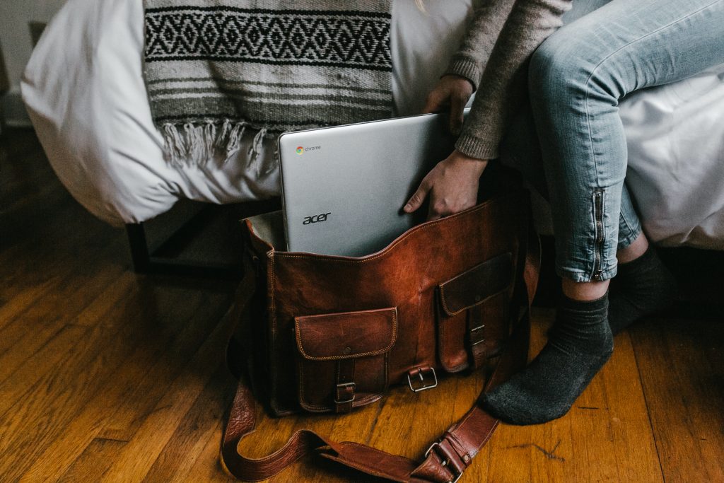 a man putting his laptop in upright position into is leather hand carry shoulder bagi a man putting his laptop in upright position into is leather hand carry shoulder bagi
