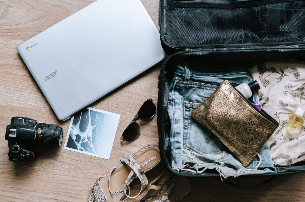 flat lay shot of an opened luggage with clothes and a toiletry bag. Next to the luggage is a laptop, a pair of shades and a ohotograph flat lay shot of an opened luggage with clothes and a toiletry bag. Next to the luggage is a laptop, a pair of shades and a ohotograph