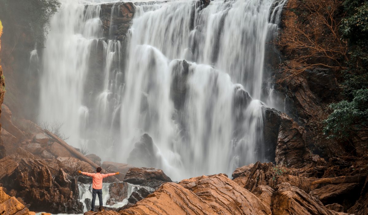 manoj kulkarni-RS_va2HSthI-unsplash aerial view of waterfall and a man admiring it with arms wide open