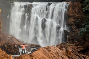 aerial view of waterfall and a man admiring it with arms wide open