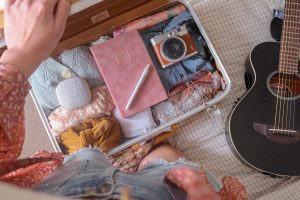 a top view shot of a luggage filled with clothes, a pink diary, a camera and a pair of shades