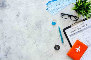 Documents for travel abroad. Visa application form, pen, passport cover with airplane silhouette on grey background top view.