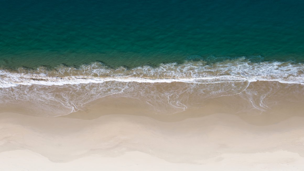 Top view of Bruny Island shore with clear white sand and turquoise water splashing on shore