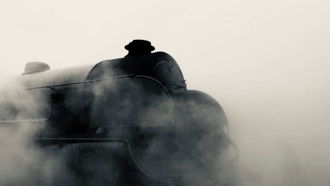 Photo of a black steam train with the whole background and foreground covered in grayish white mist and smoke