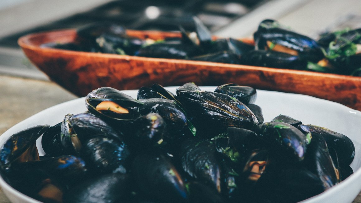 Photos of mussels in a white ceramic bowl and a wooden brown bowl on a table